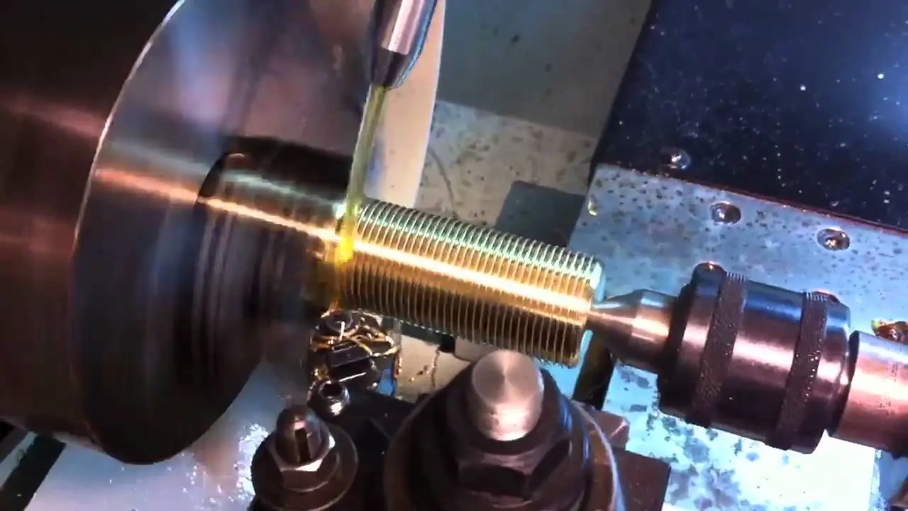 A metal lathe machining a threaded brass cylinder.