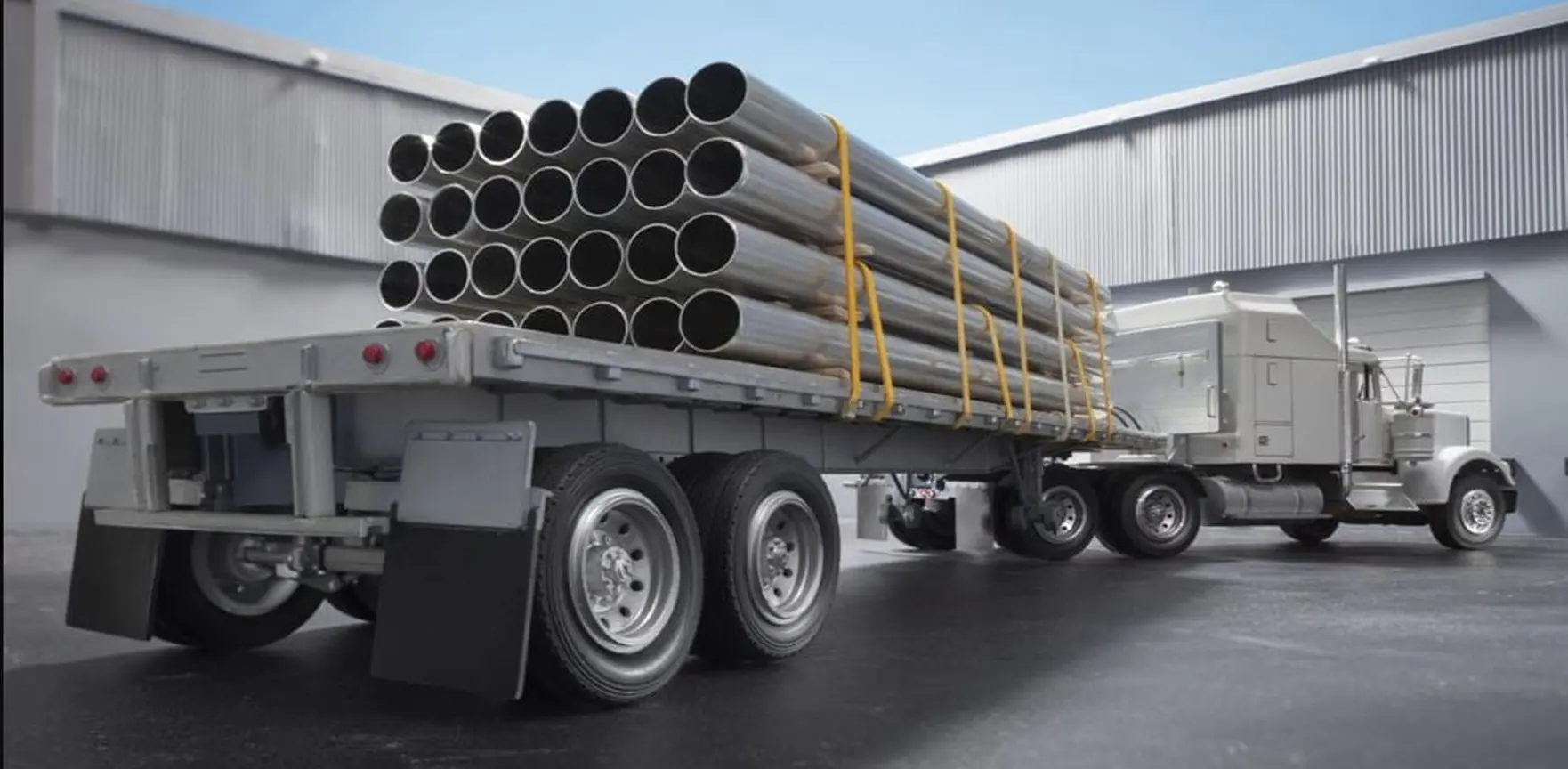 Flatbed truck loaded with steel pipes secured by yellow straps.