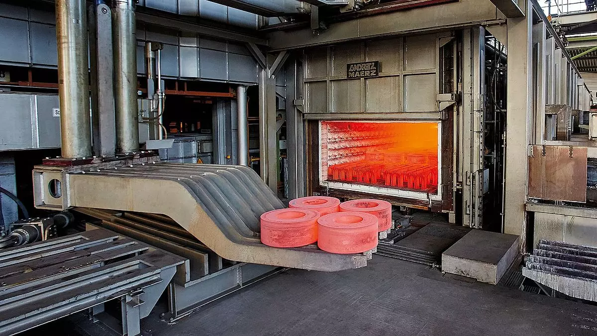 Industrial furnace with glowing hot metal discs on a conveyor.