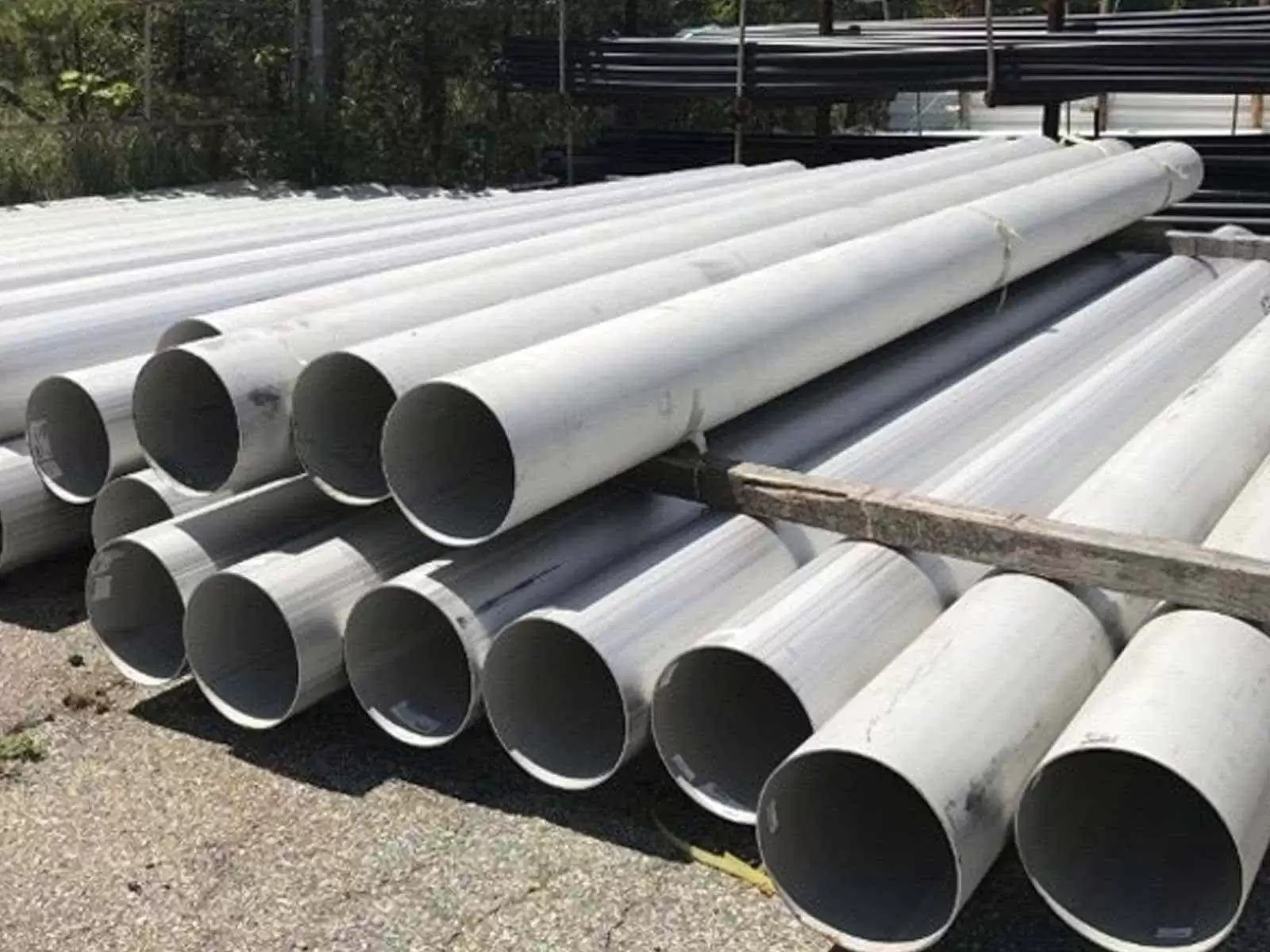 Stacked white PVC pipes outdoors on the ground.